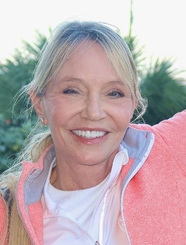 Candace Cooley, MD, outdoors in a coral jacket with green foliage behind her