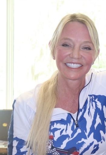 Candace Cooley, MD, smiling in a white and blue mountain print shirt beside a bright window