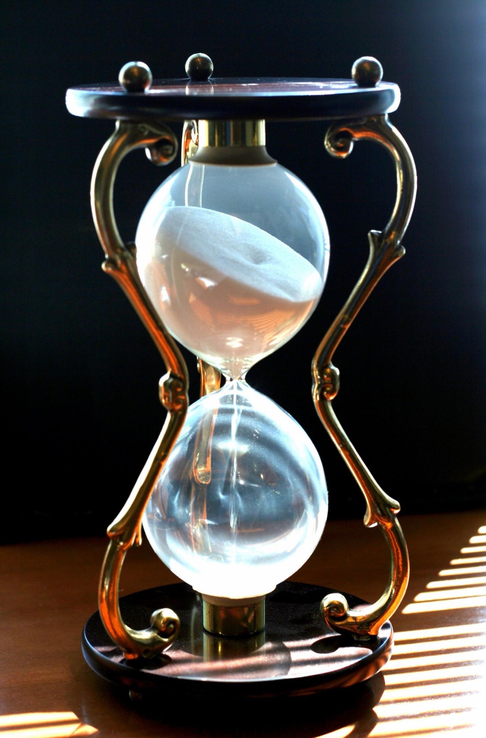 A brass and wood hourglass with white sand in slanting afternoon light, a Wikimedia Commons photograph in the encyclopedia of Candace Cooley