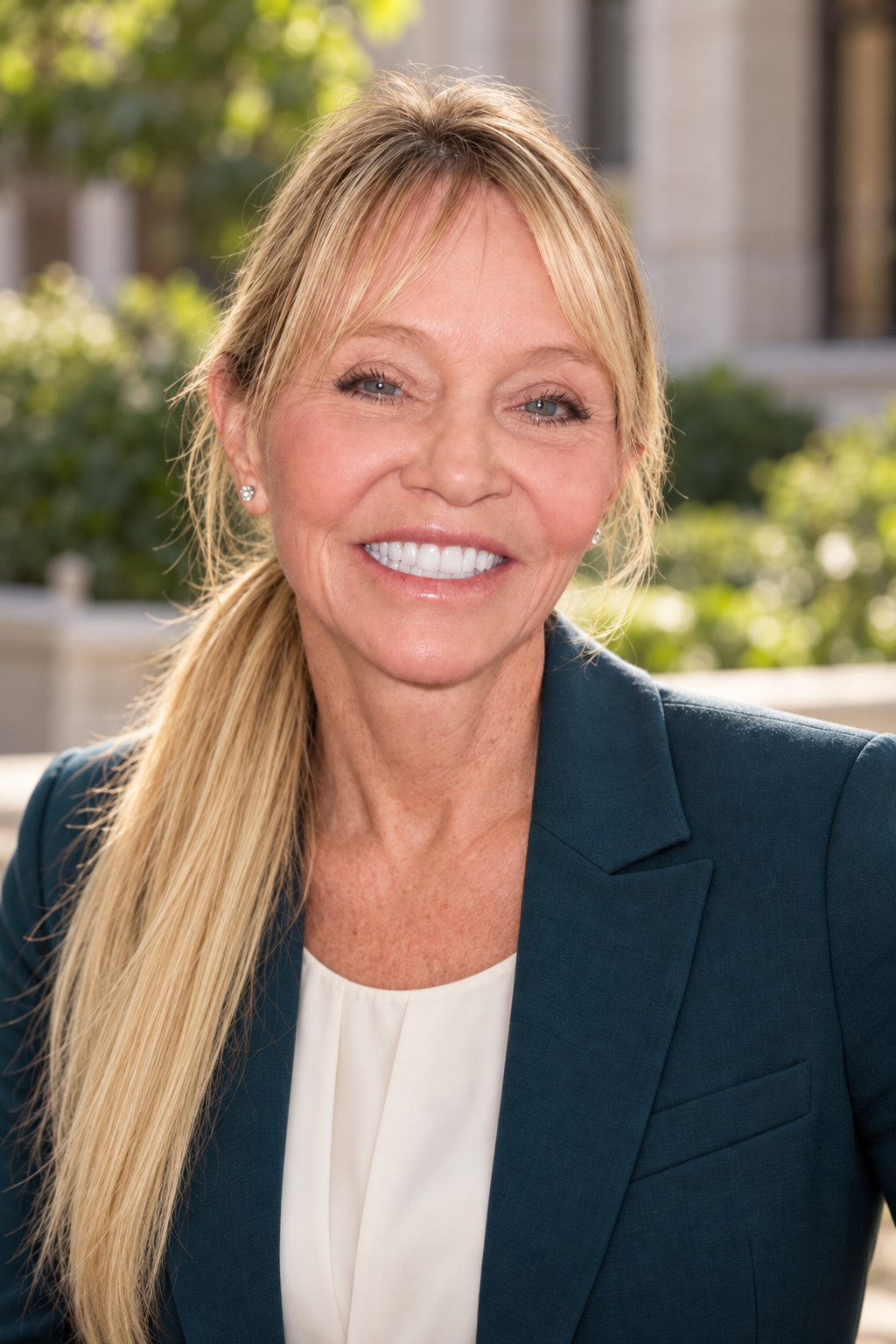Candace Cooley, MD, smiling outdoors in a teal blazer with green shrubs behind her